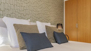 A hotel room with a bed, pillows, a wardrobe, and a patterned wallpaper.