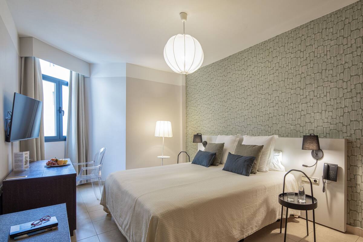 Habitación de hotel con una cama grande, un escritorio con televisor, una lámpara y un teléfono en la pared.