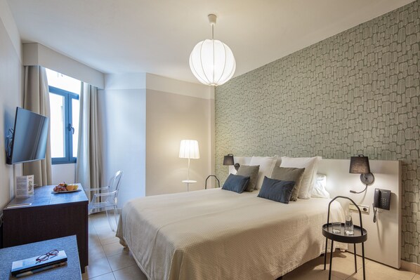 Habitación de hotel con una cama grande, un escritorio con televisor, una lámpara y un teléfono en la pared.