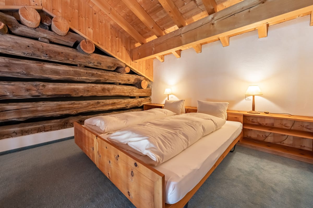 A wooden bed in a cabin-style room with a log wall and two bedside lamps.