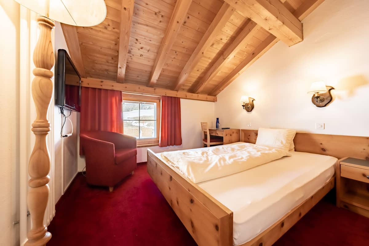 A wooden-framed bedroom with a bed, a desk, a chair, and a TV.