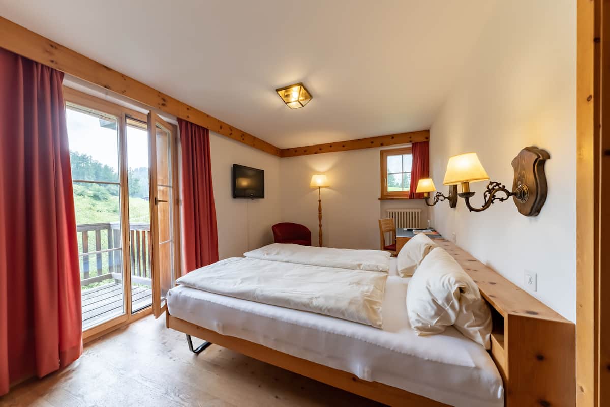 A bedroom with a wooden bed, a red chair, a desk, a lamp, and a view of the outdoors.