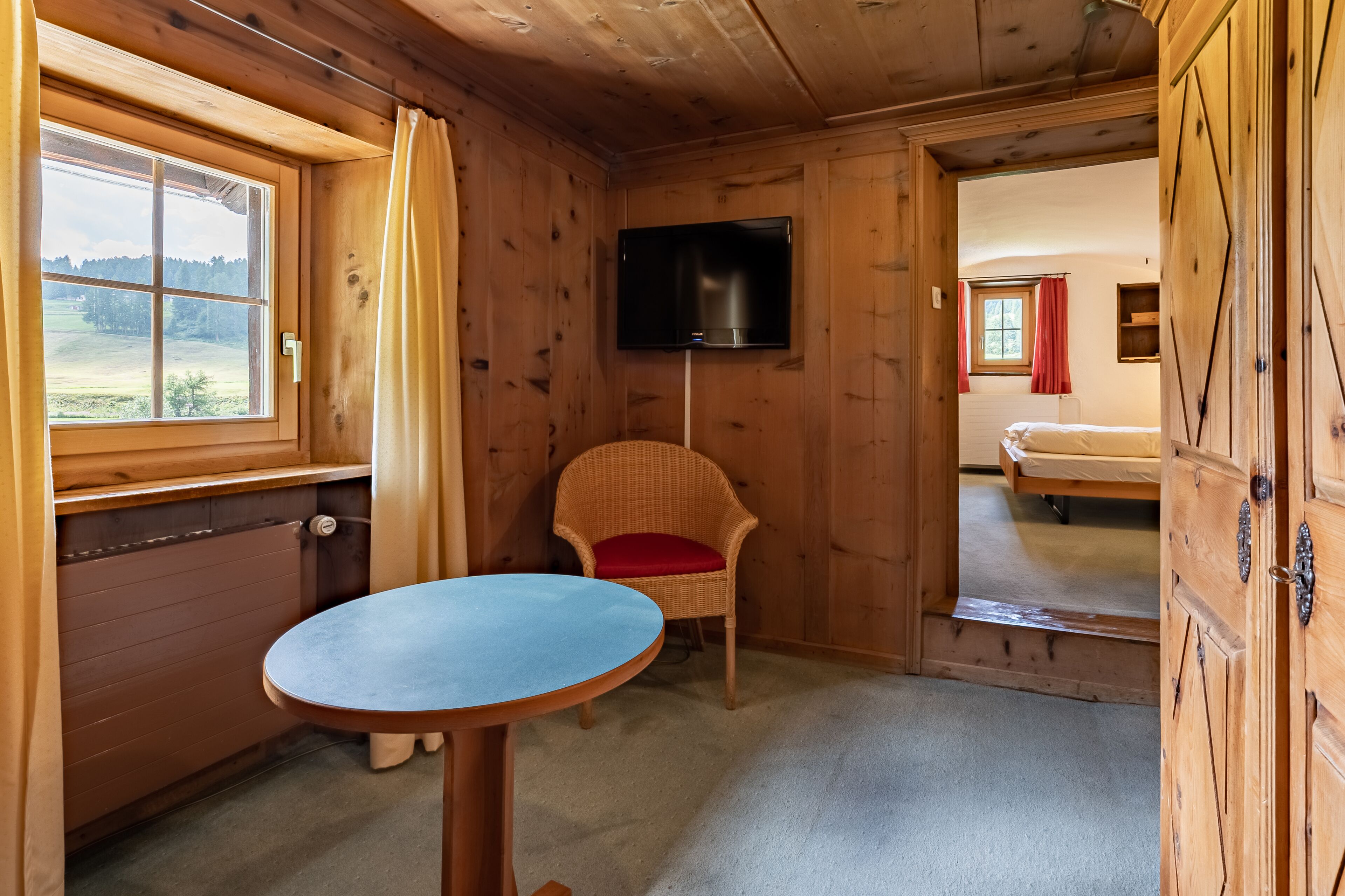 Een houten kamer met een bed, een tafel, een stoel en een televisie.