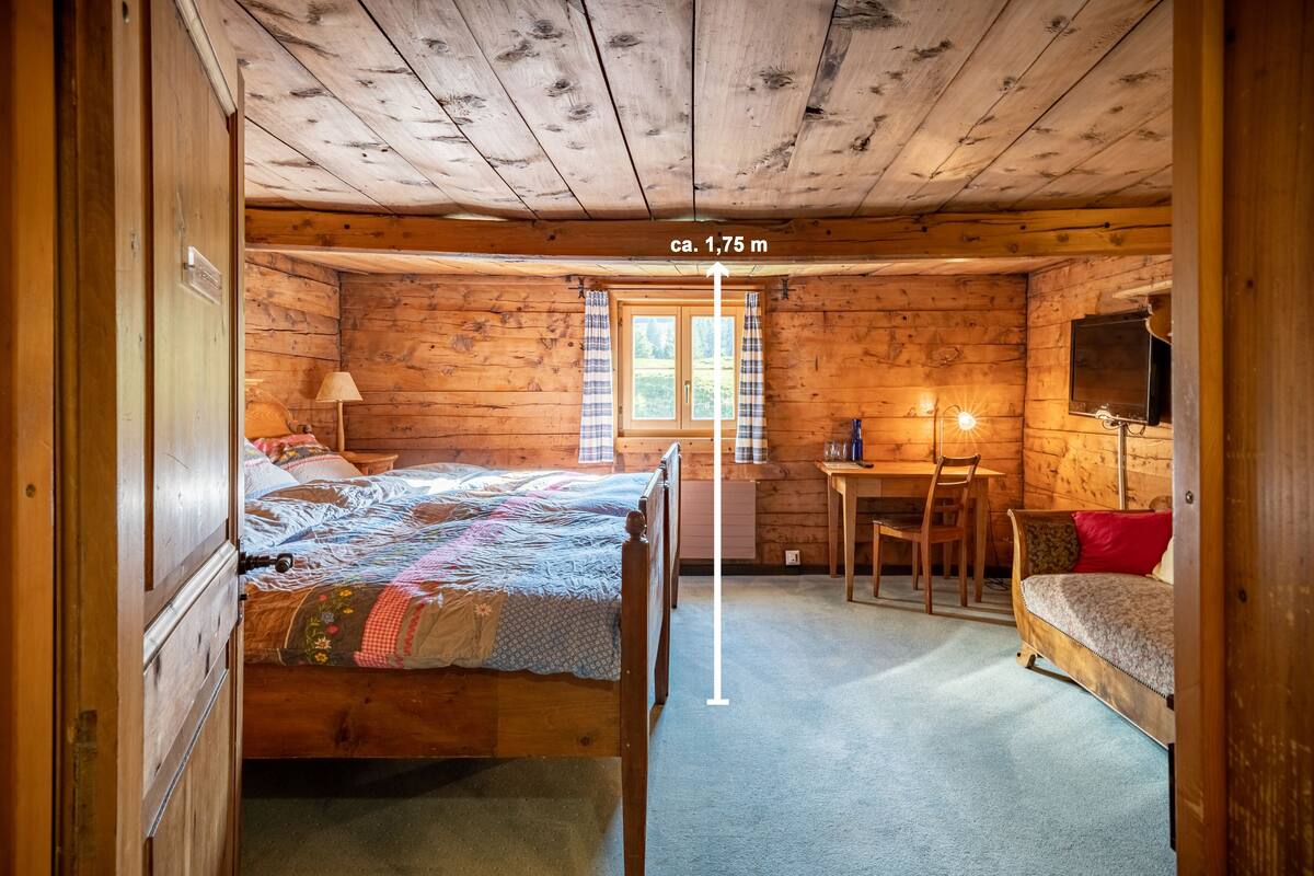 A wooden cabin room with a bed, a desk, and a sofa.