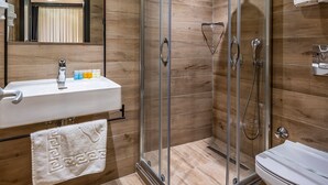 Un baño moderno con ducha de vidrio, lavamanos con artículos de aseo y retrete.