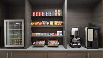 A self-service beverage station with a refrigerator, coffee machine, and snack dispensers.