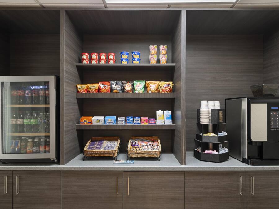 A self-service beverage station with a refrigerator, coffee machine, and snack dispensers.