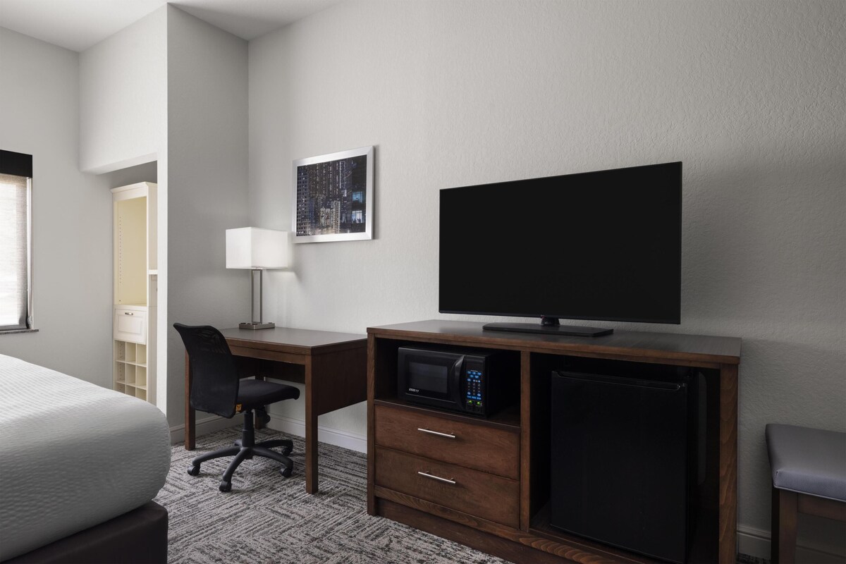 A hotel room with a bed, a desk with a chair, a flat-screen TV, a microwave, and a mini-fridge.