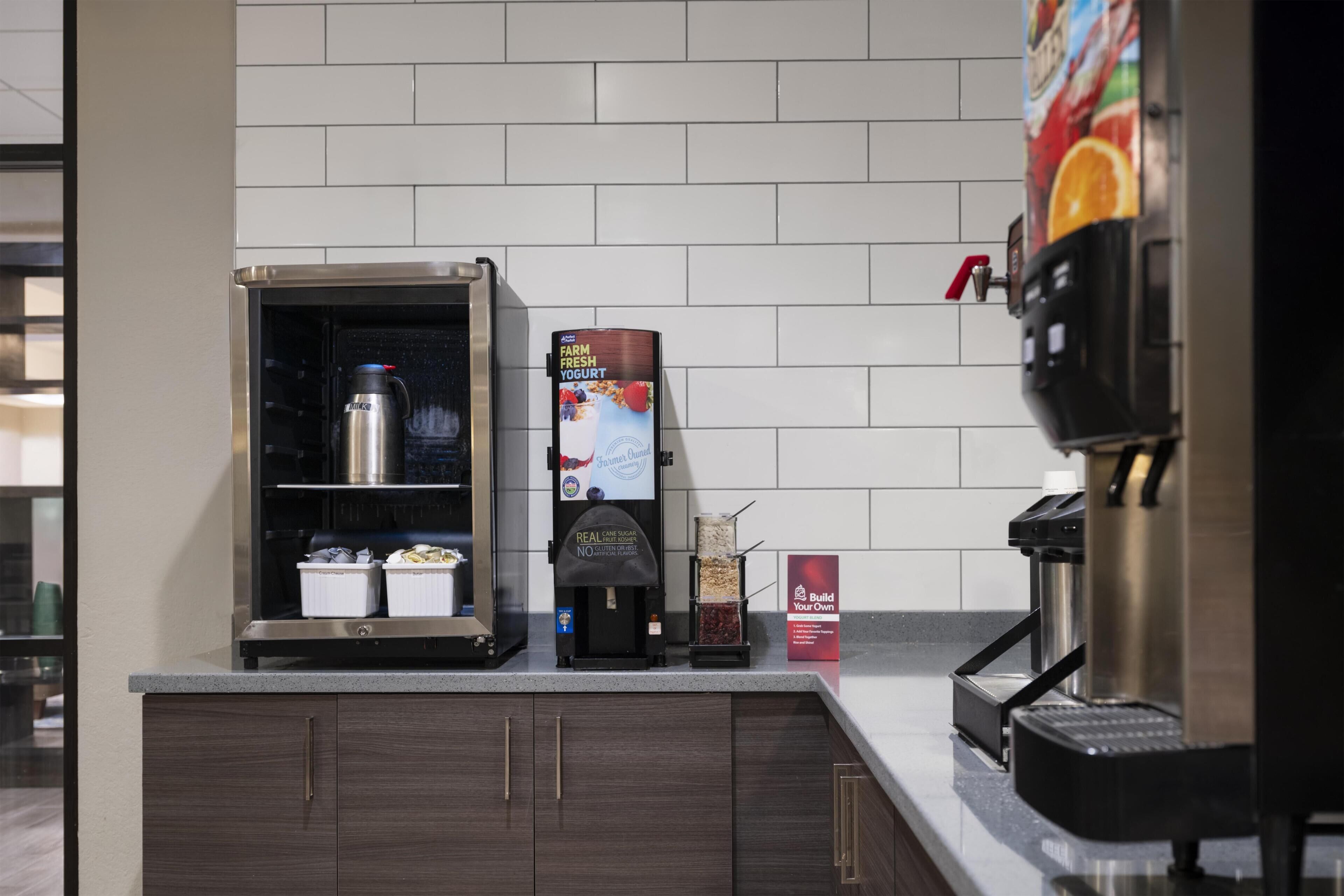 A coffee station with a coffee machine, a milk frother, and a sign for 'Farm Fresh Yogurt.'