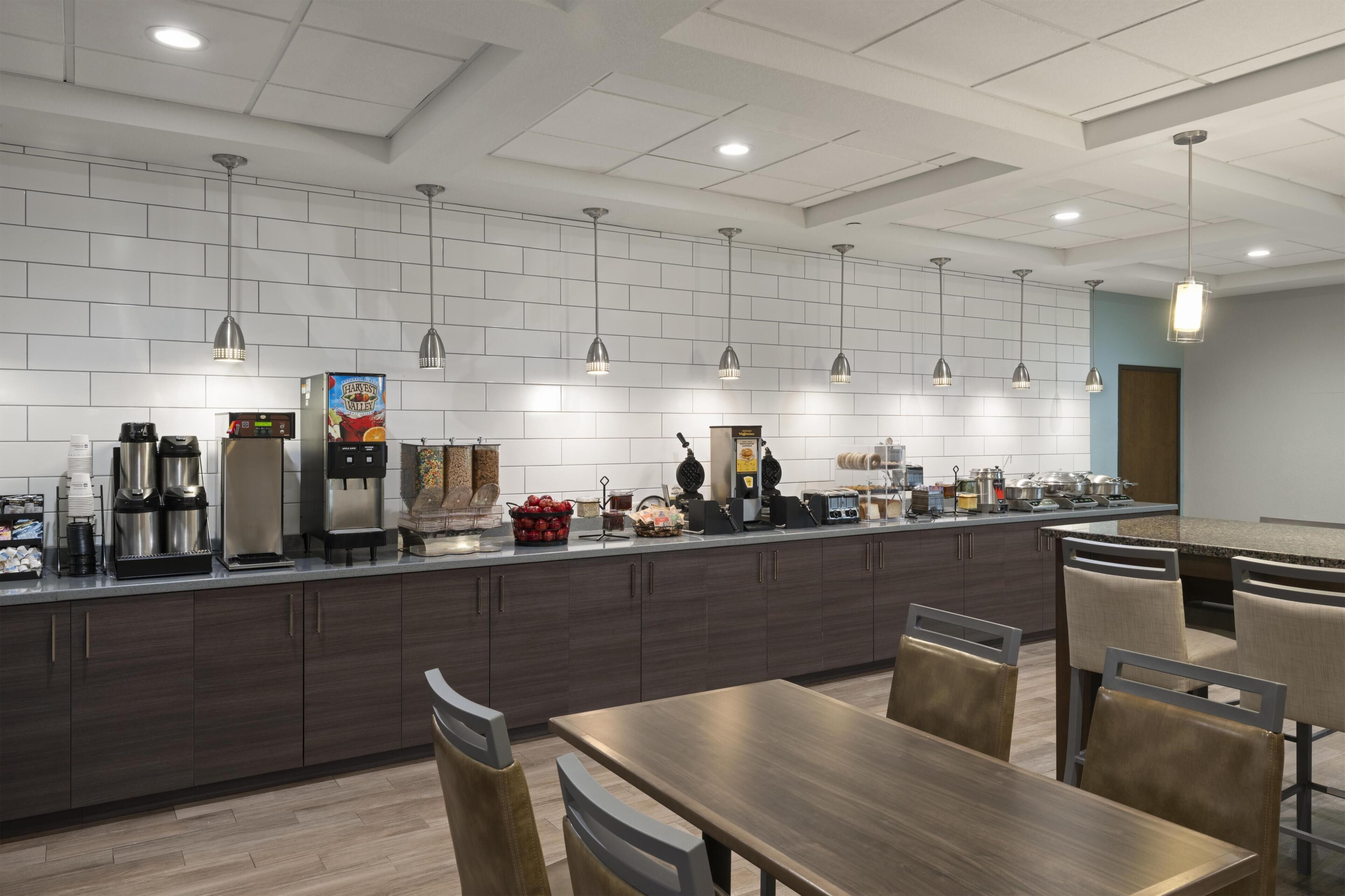 A modern kitchen with a long counter, coffee machines, and a seating area with tables and chairs.