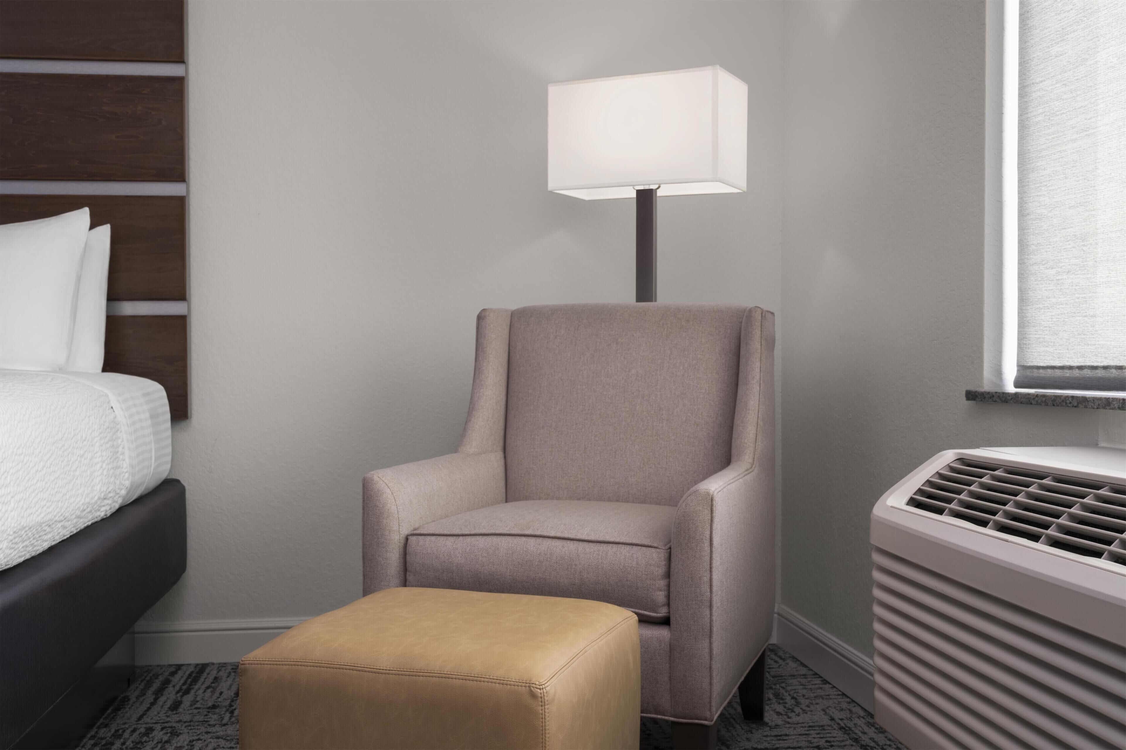 A hotel room with a bed, a chair, a table, a lamp, and a radiator.