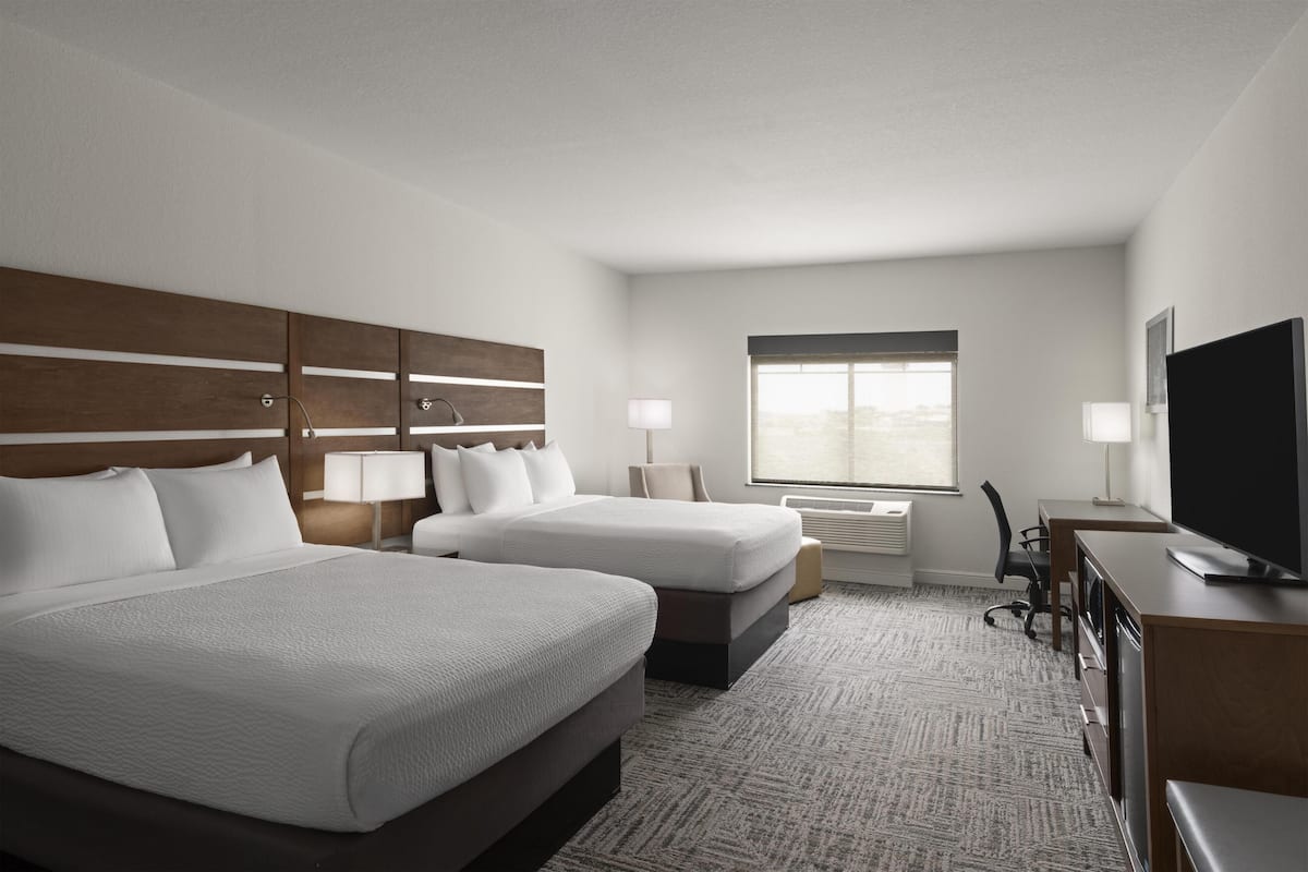 A hotel room with two beds, a desk, a television, and a window with a view.