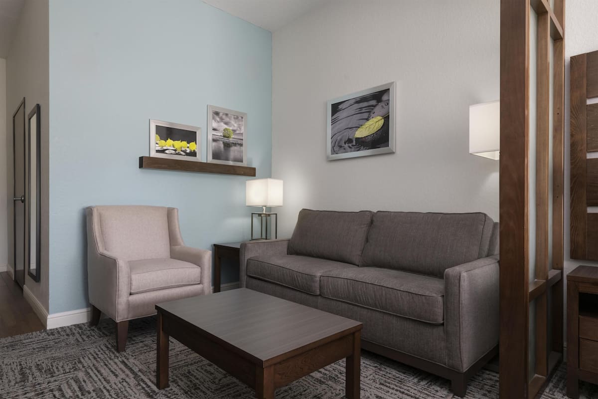 A living room with a sofa, armchair, coffee table, and wall-mounted lamp.