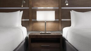 A hotel room with two beds, a nightstand with a lamp, and wooden paneling on the wall.