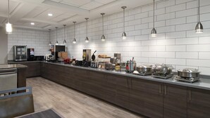 A modern kitchen with a long counter, overhead pendant lights, and a variety of cooking appliances.