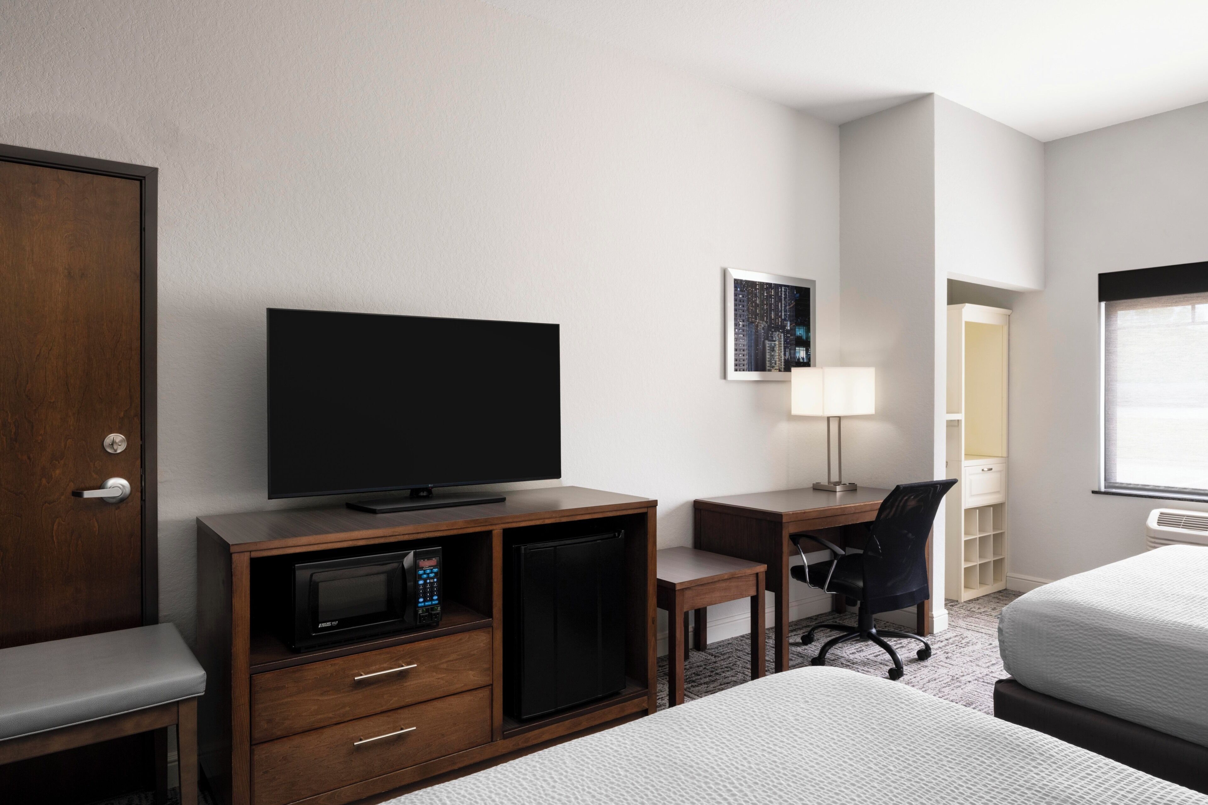A hotel room with a bed, a desk with a computer, a television, a microwave, and a door.