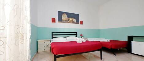 A hotel room with a bed, two bedside tables, a nightstand, a painting of the Colosseum, and a white ceiling light.