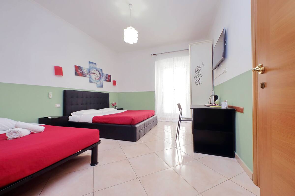 A hotel room with two beds, a desk, a chair, a TV, and artwork on the walls.
