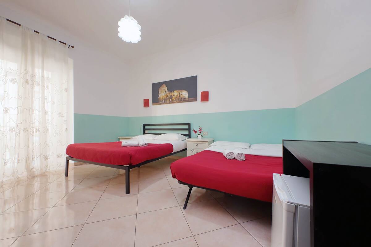A hotel room with two beds, a small desk, a television, and a painting on the wall.