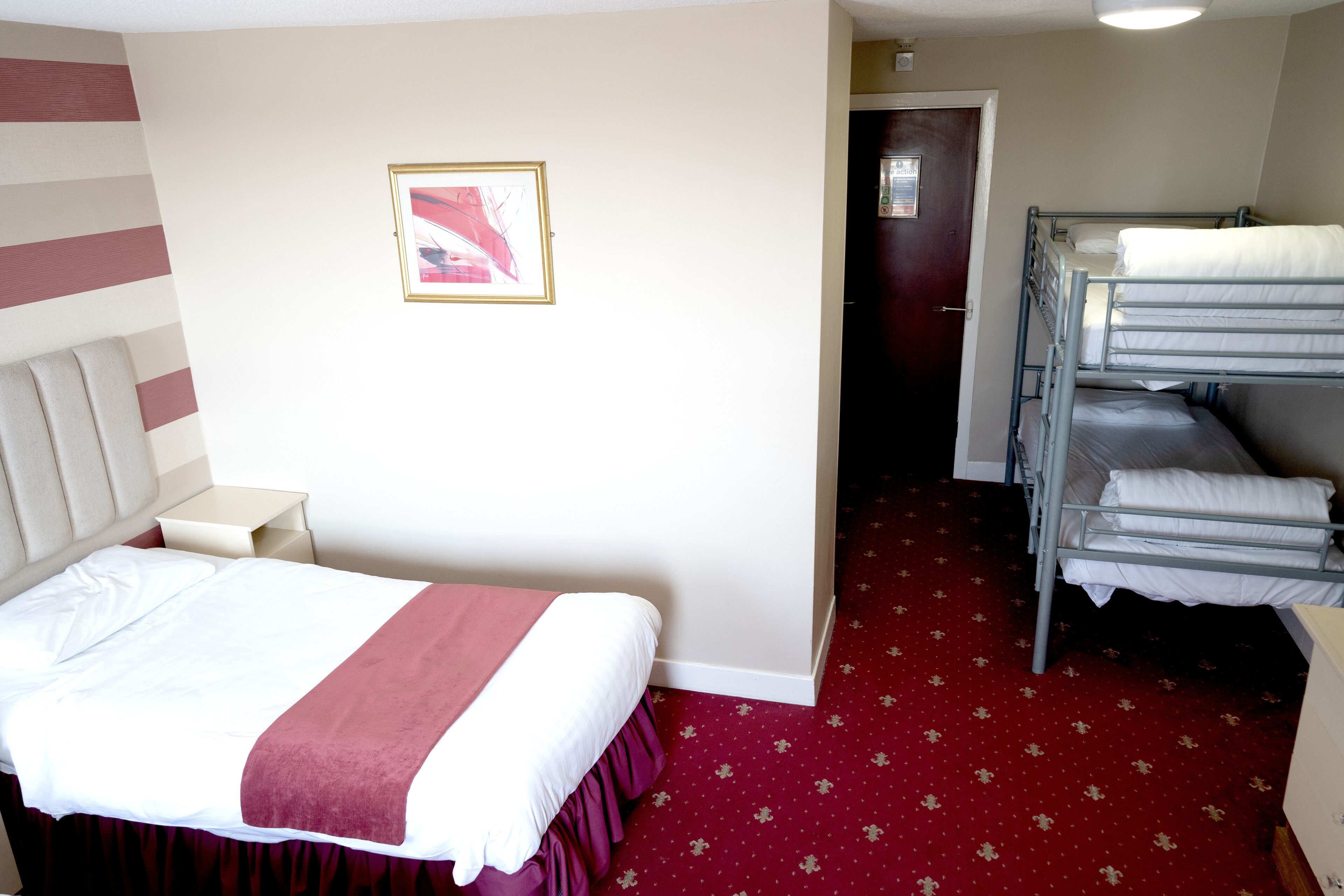 A hotel room with a single bed, a bunk bed, a small bedside table, and a framed picture on the wall.