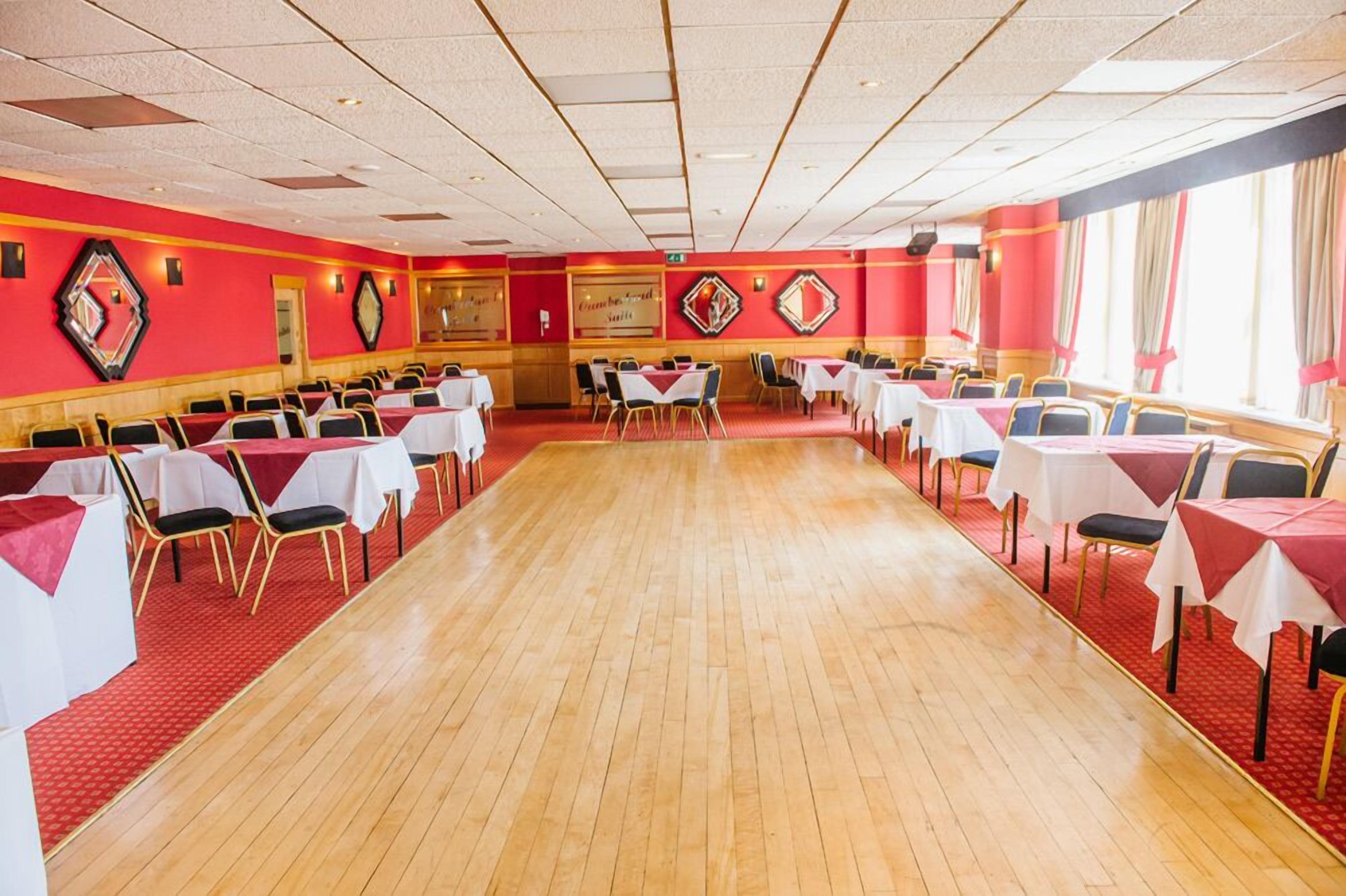 A large banquet hall with rows of tables and chairs, red walls, and a wooden floor.