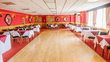 A large banquet hall with rows of tables and chairs, red walls, and a wooden floor.