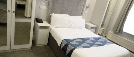 A hotel room with a bed, a bedside table with a phone, a mirror, and a door leading to a bathroom.