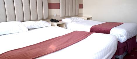 Habitación de hotel con dos camas, cada una con una manta roja, cabeceros, mesitas de noche y un teléfono.