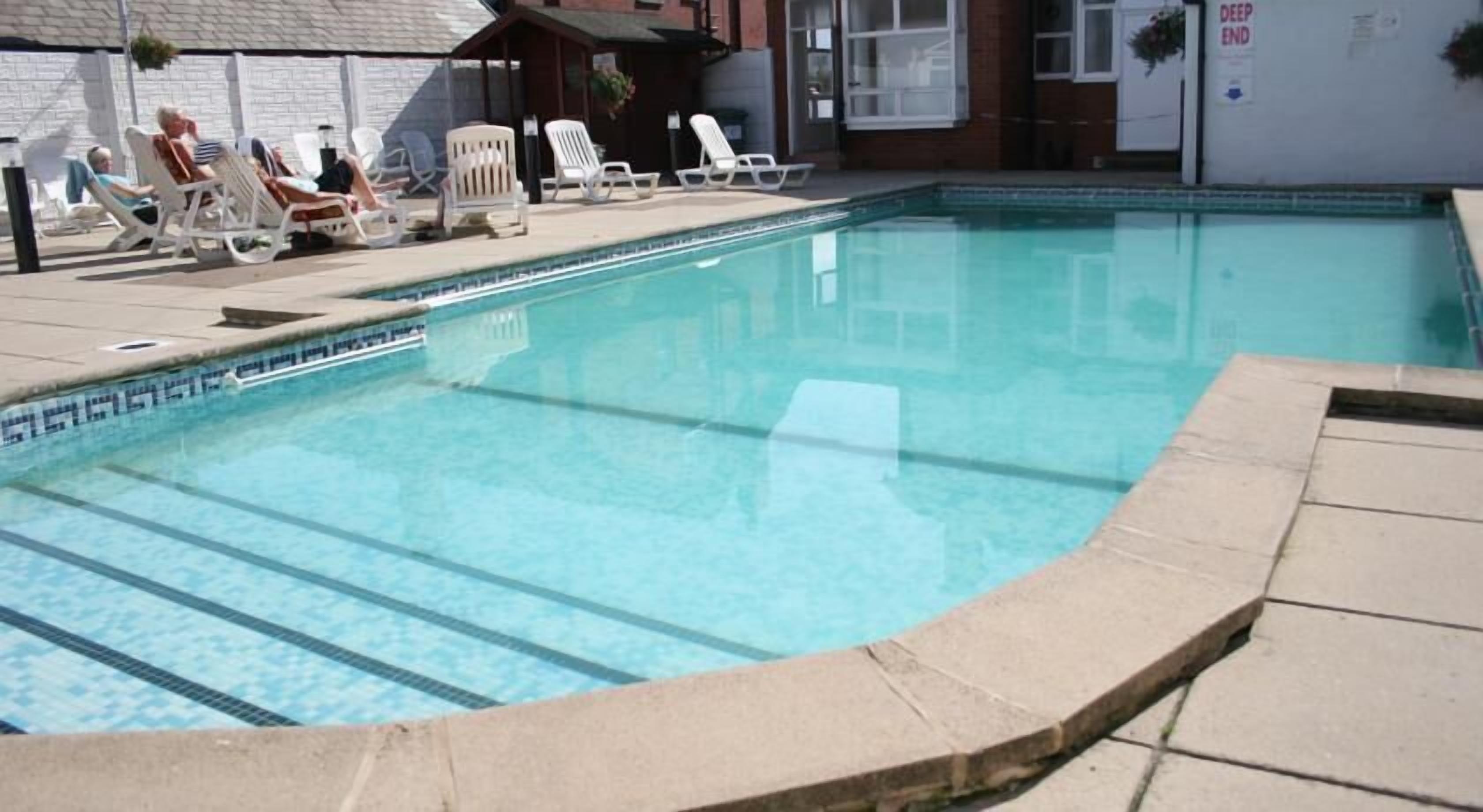 A swimming pool with lounge chairs and a covered area.