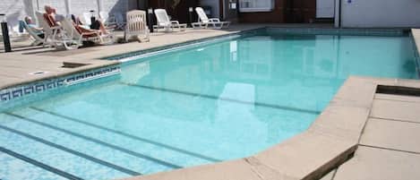 A swimming pool with lounge chairs and a covered area.