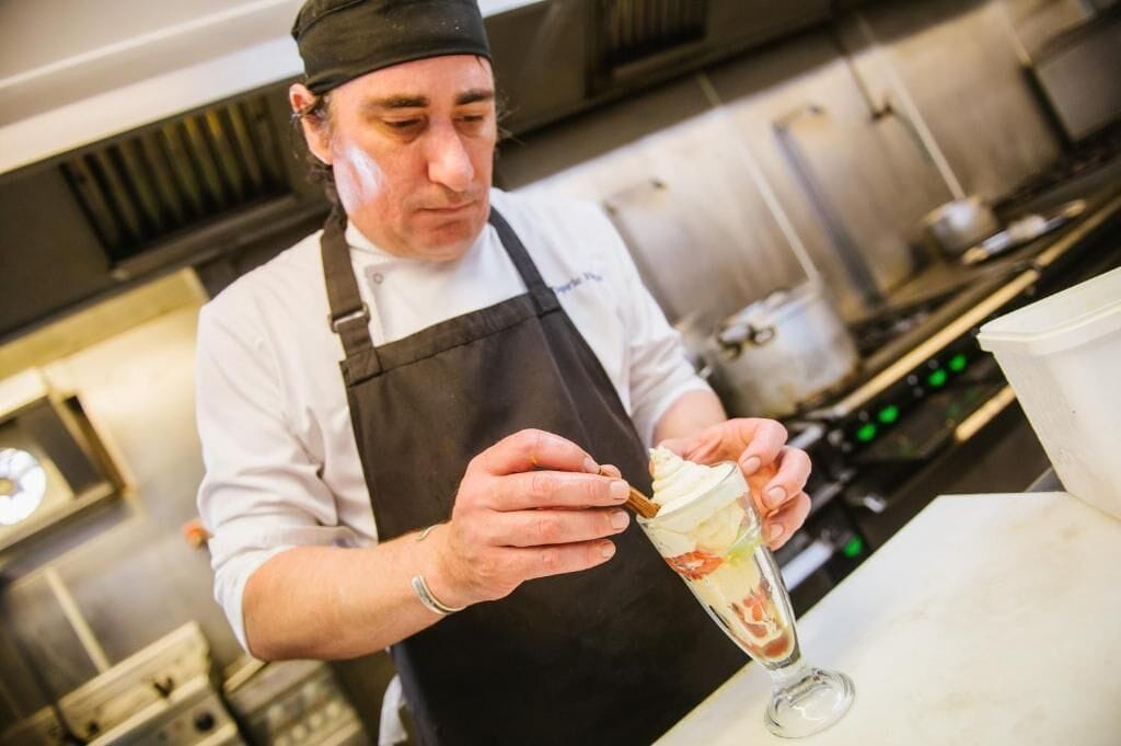 A chef in a professional kitchen preparing a dessert.