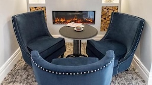 Una habitación con dos sillones tapizados en azul, una pequeña mesa redonda, una chimenea y estanterías decorativas con jarrones.