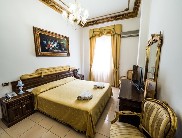 Une chambre d’hôtel avec un grand lit, une table de chevet avec un téléphone, une chaise, un bureau avec une télévision et un miroir.