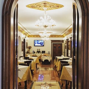 Une salle à manger avec des tables dressées, un lustre et un téléviseur fixé au mur.