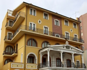 Un immeuble jaune doté de nombreux balcons et d’une entrée centrale sur laquelle est apposée une enseigne indiquant « 2003 EURO HOTEL ROSOLINI IGLIESIAS ».