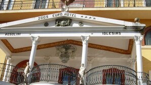 Un edificio con un balcón, un letrero que dice "2005 EURO HOTEL" y una estatua en el balcón.
