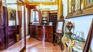 Un lobby lujoso con piso de mármol, una recepción, detalles ornamentales dorados y obras de arte enmarcadas.