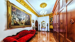 Una habitación con un sofá rojo, un cuadro grande enmarcado, armarios de madera y un candelabro.