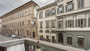 A balcony with a bottle of wine and glasses, overlooking a street with historic buildings.