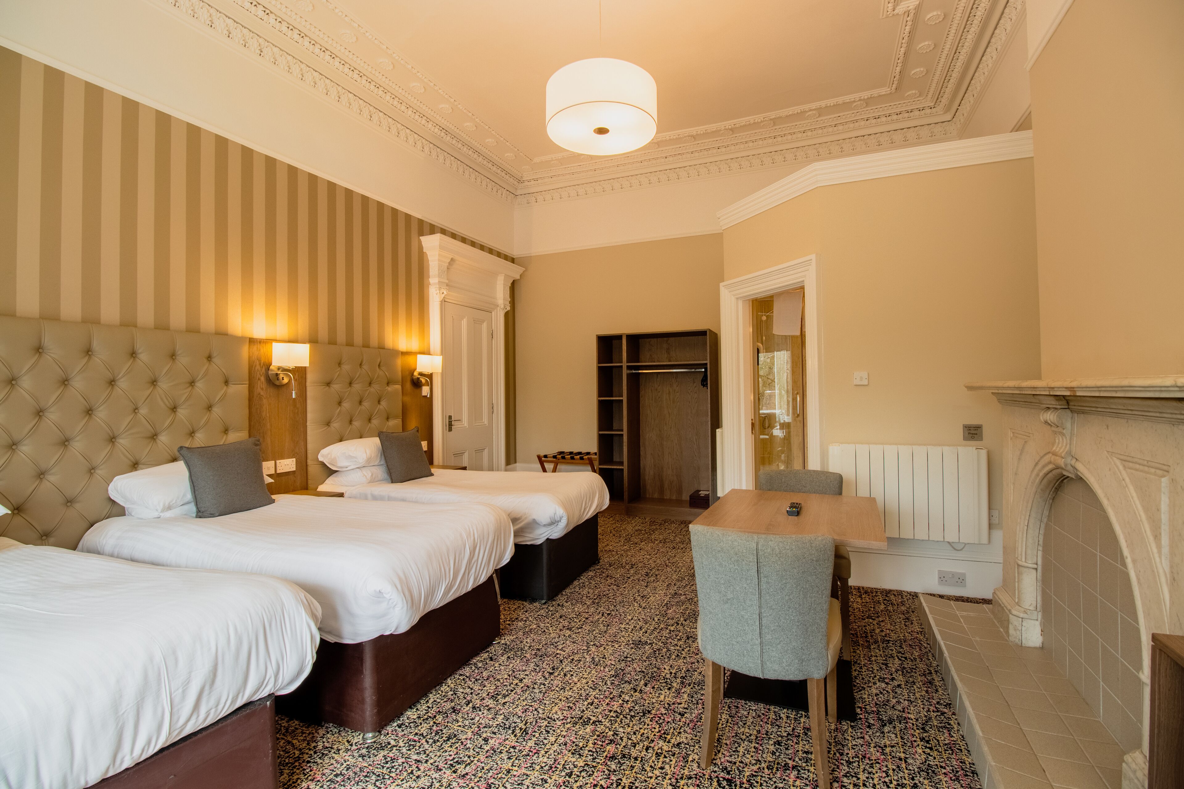 A hotel room with three beds, a dining table, a fireplace, and a large mirror.