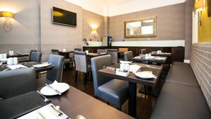 Un restaurant avec des tables et des chaises, un grand miroir et des lampes fixées au mur.