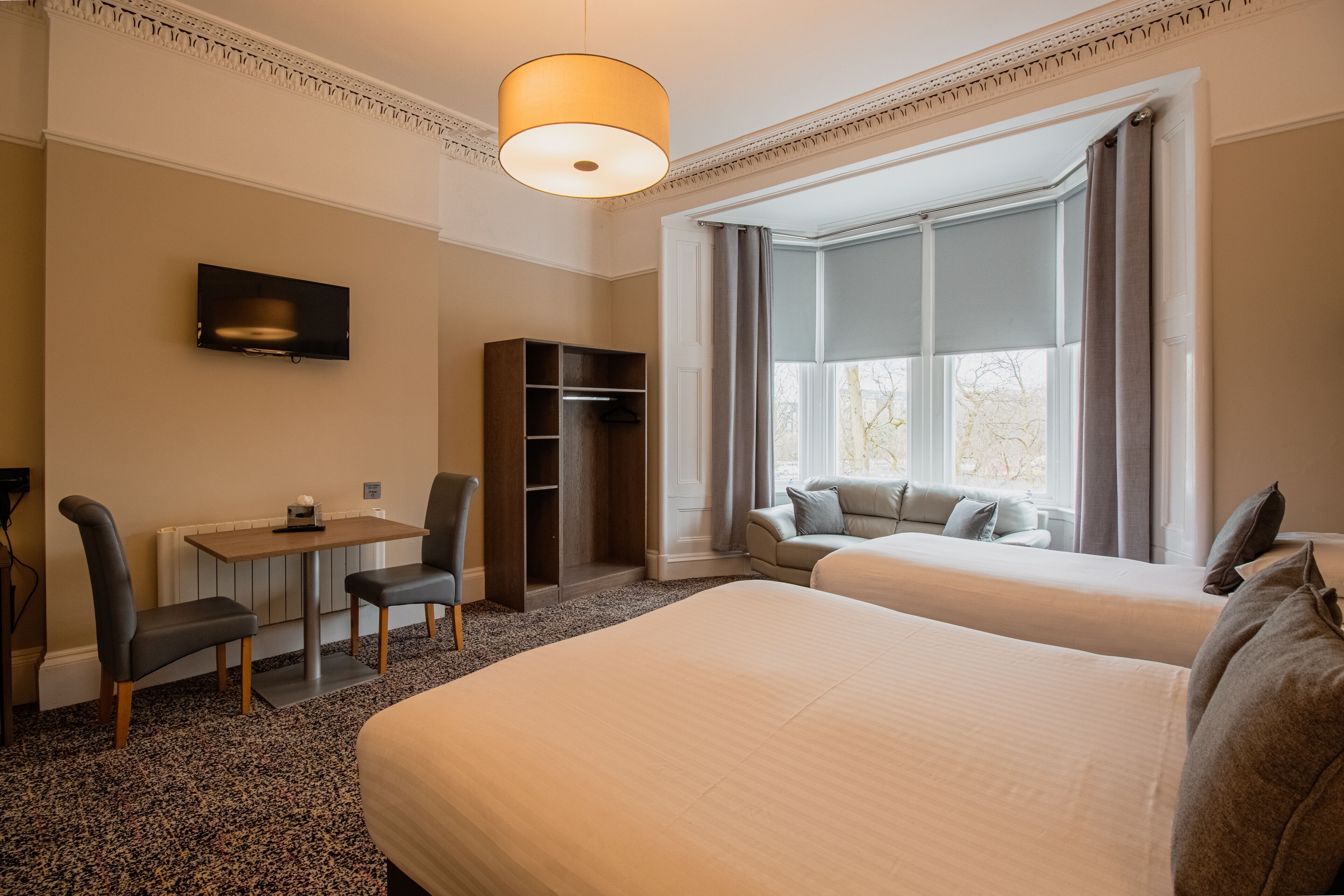 Une chambre d’hôtel avec deux lits, un bureau avec une chaise, une télévision et une armoire.