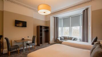 Una habitación de hotel con dos camas, un escritorio con silla, un televisor y un armario.