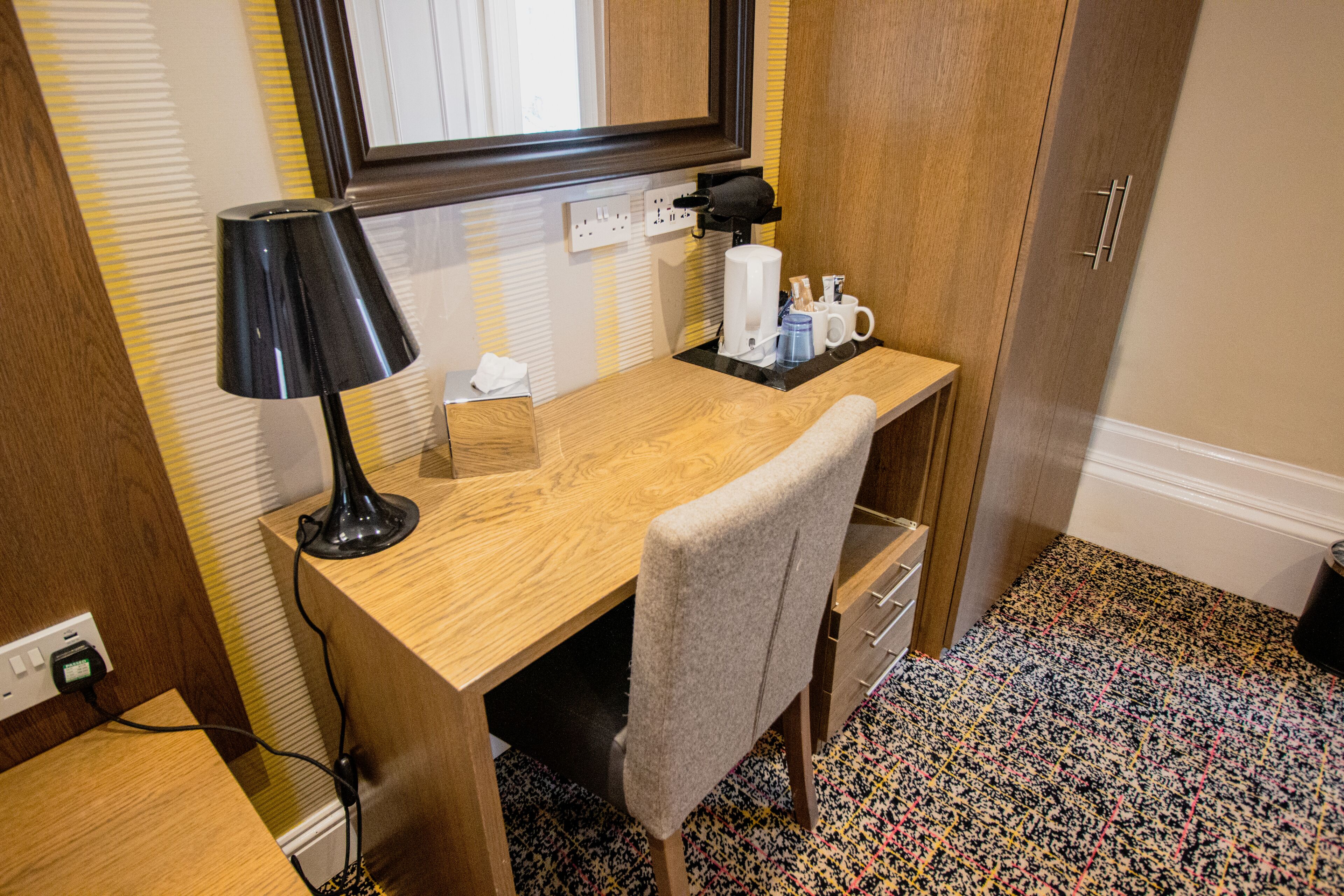 Un espacio de trabajo pequeño con un escritorio de madera, una lámpara, una silla y una máquina de café.