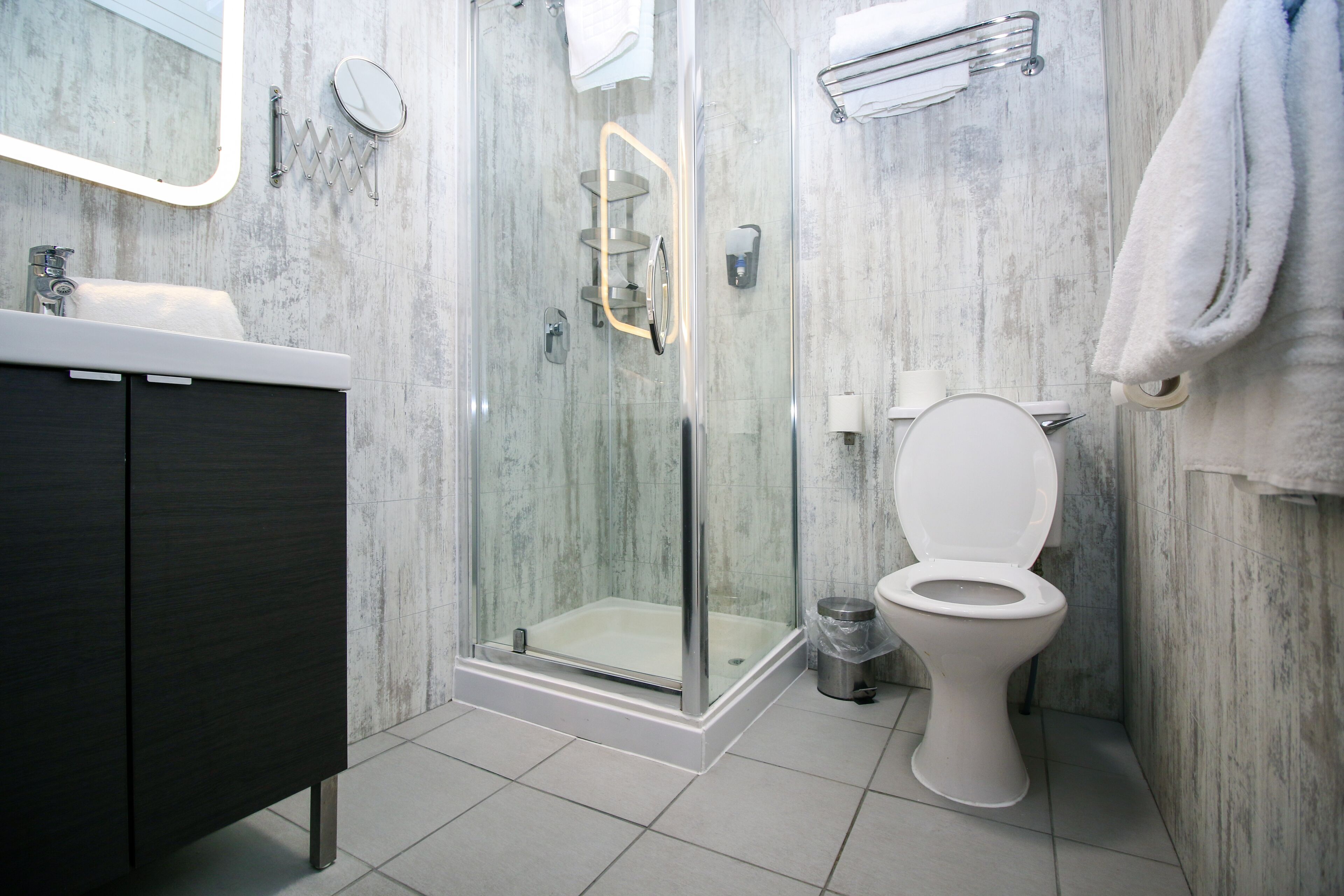 Une salle de bain moderne avec une douche à parois de verre, des toilettes blanches et un meuble-lavabo de couleur foncée.