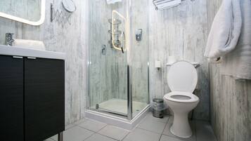 Et moderne badeværelse med en glasafskærmet bruseniche, et hvidt toilet og en mørk kommode.