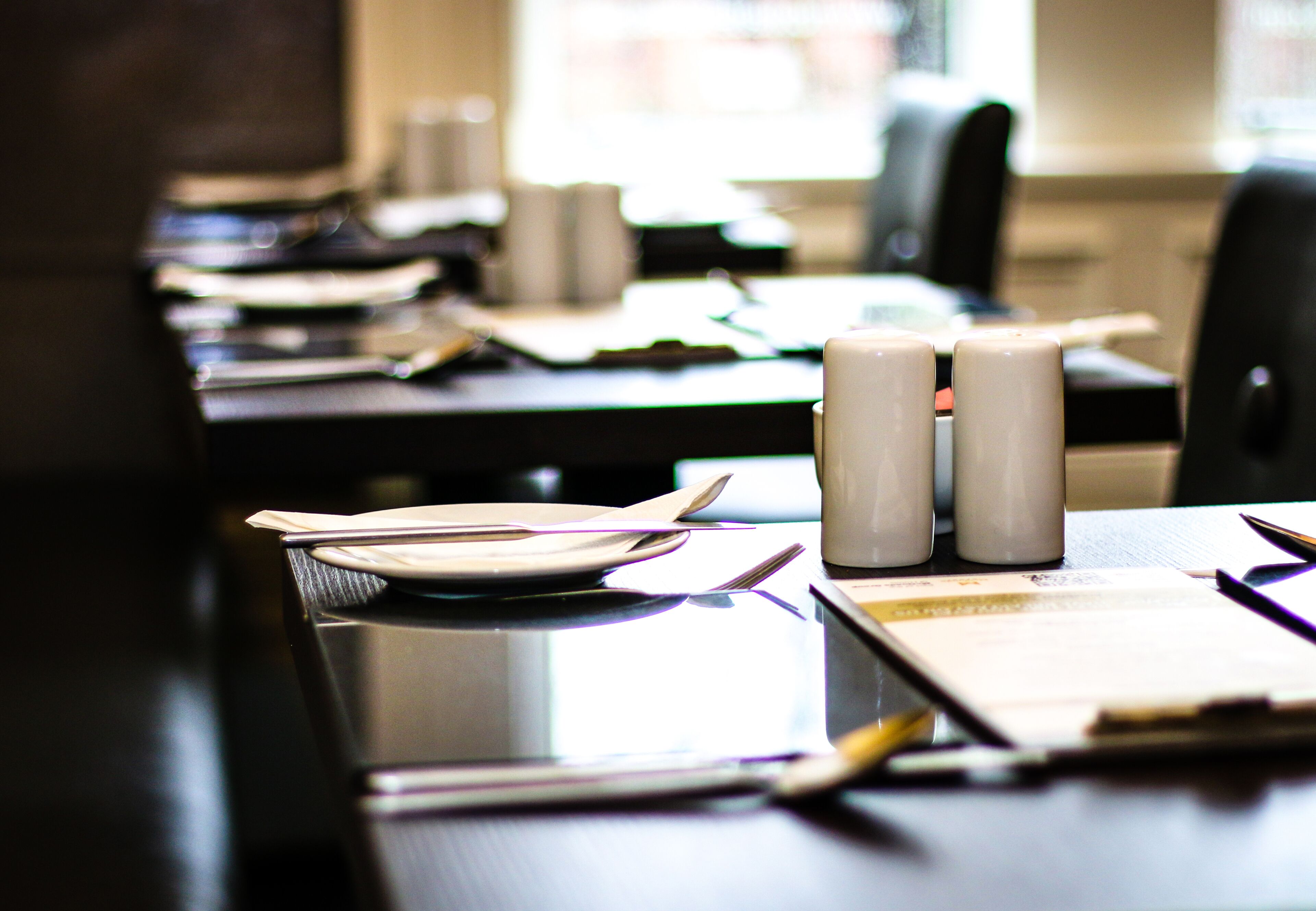 A dining table with plates, cutlery, salt and pepper shakers, and a notebook.
