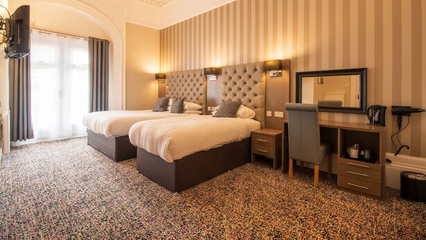 Une chambre d’hôtel avec deux lits, un bureau avec une chaise, un miroir et un téléviseur.