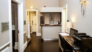 Un espace d’accueil d’hôtel avec un comptoir à carreaux, un bureau avec un ordinateur et une imprimante, et une lampe fixée au mur.