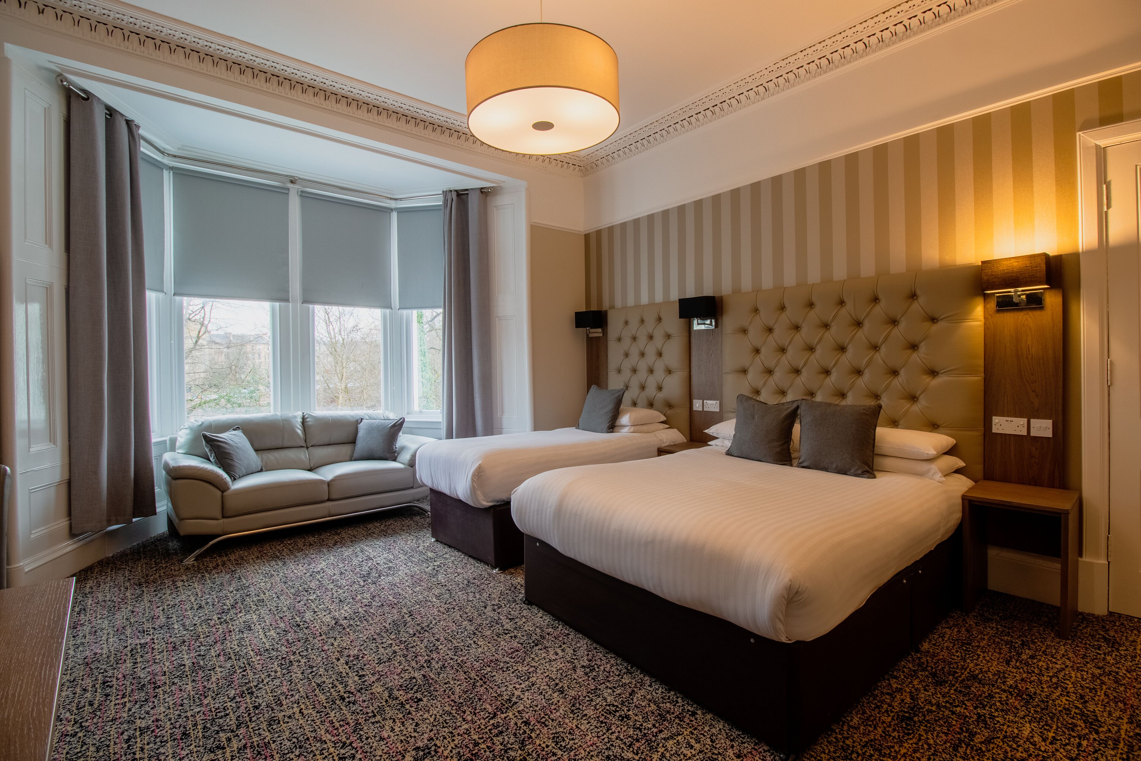 A hotel room with two beds, a sofa, a large window, and a striped wall.